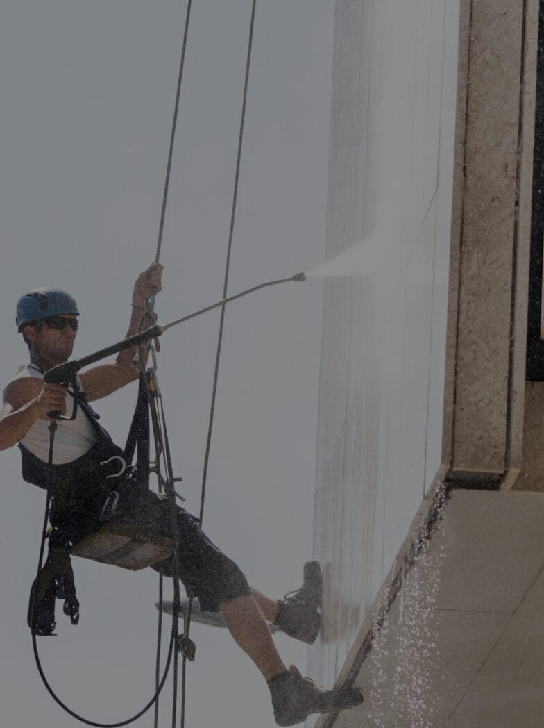 Worker cleaning building with pressure washer.