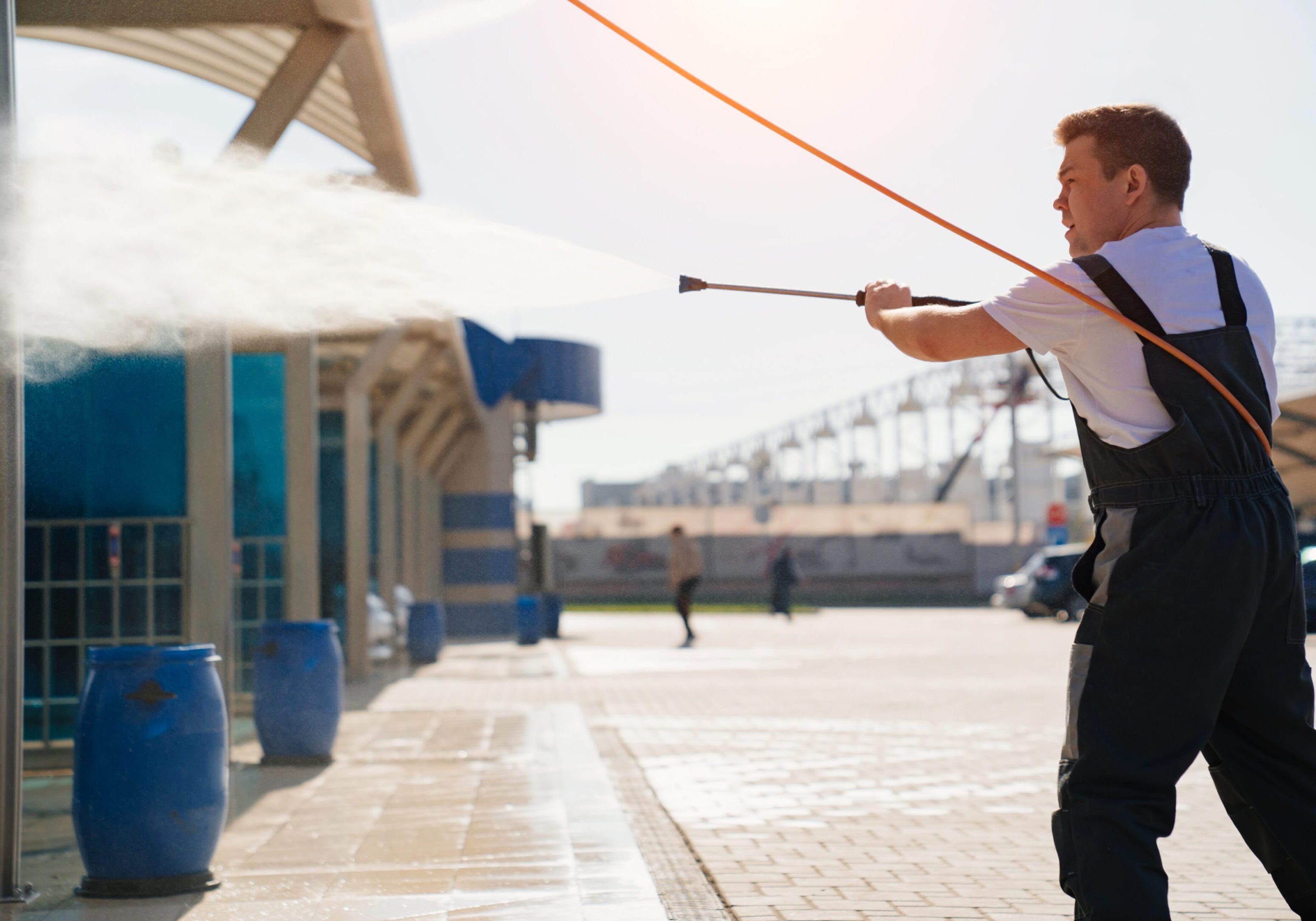 self-service car wash. a man in a work jumpsuit washes the car from a hose. Man pressure washing a building exterior.